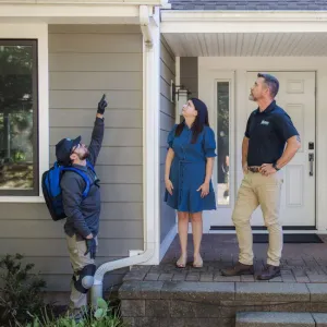 two technicians and customer looking up at front of home exterior