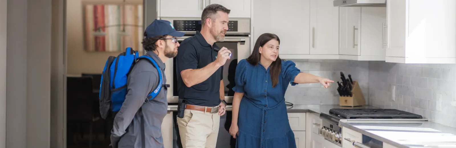 technicians and customer in kitchen pointing towards pest issue